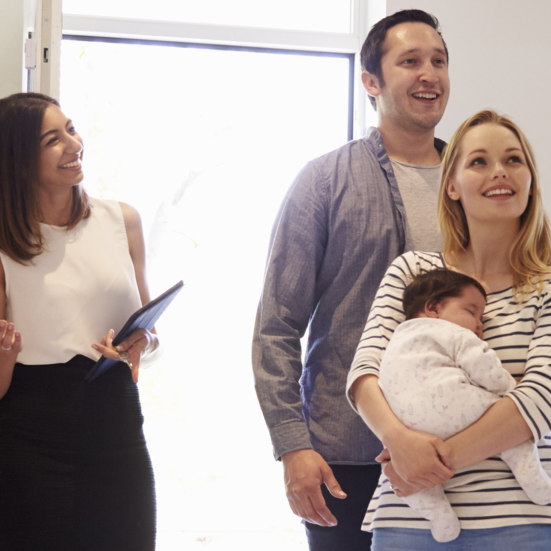 Image of a realtor showing a house to a young couple with a baby