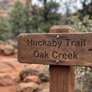A close-up photograph of a hiking trail sign in Sedona. A close-up photograph of a wooden hiking trail sign in Sedona for "Huckaby Trail" and "Oak Creek".